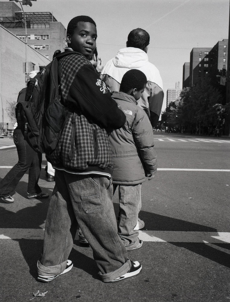 photographie en noir et blanc argentique, vintage. Un adolescent noir attend le passage du marathon de New York sur une avenue de Harlem. Obama 2008