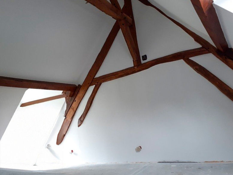 Travaux d'isolation / plâtrerie, Poutres en bois rustiques soutenant un plafond mansardé blanc et lumineux.