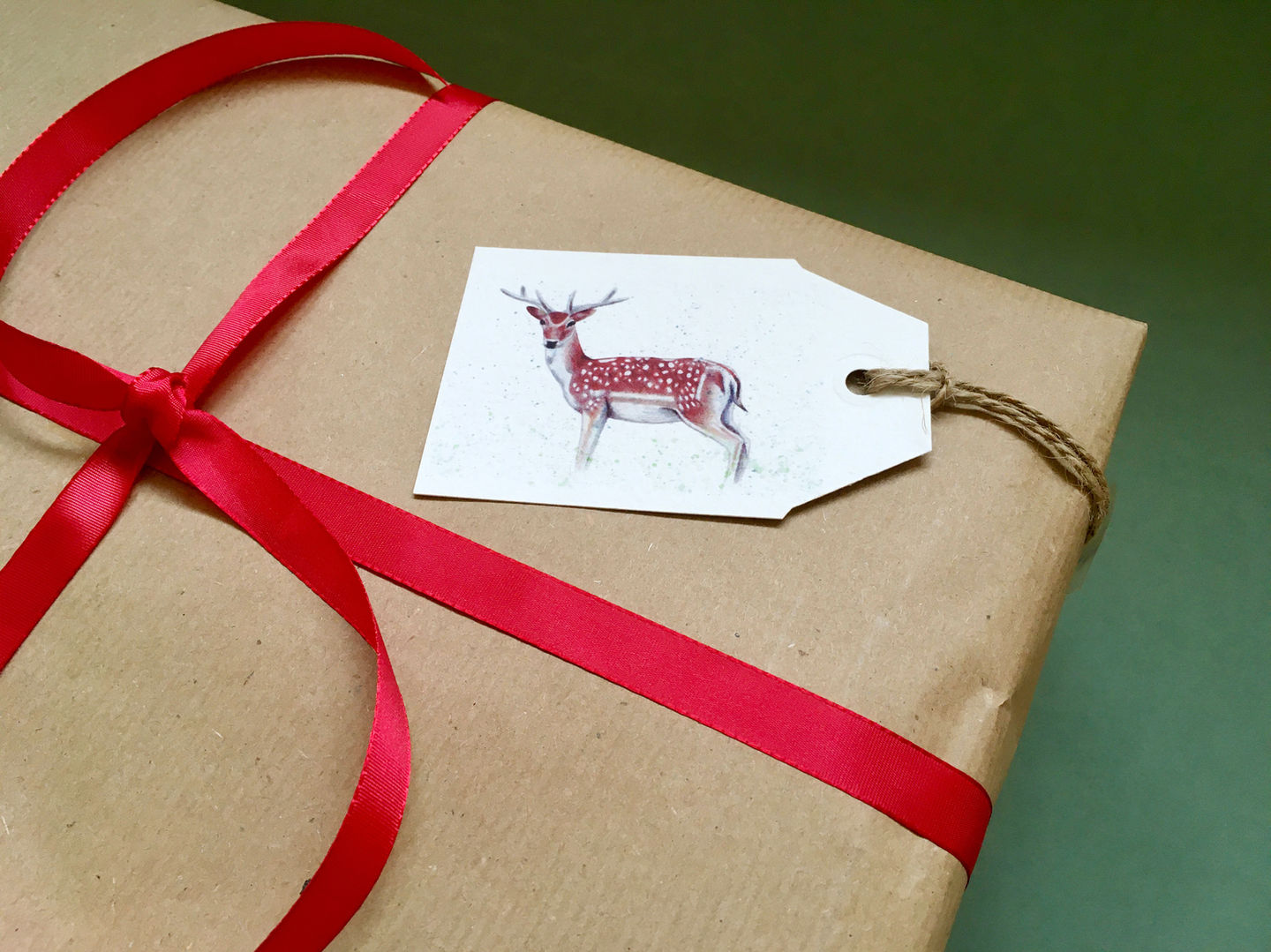 A deer gift tag on a wrapped Christmas present. The wrapping paper is brown kraft paper and it is wrapped with red ribbon.