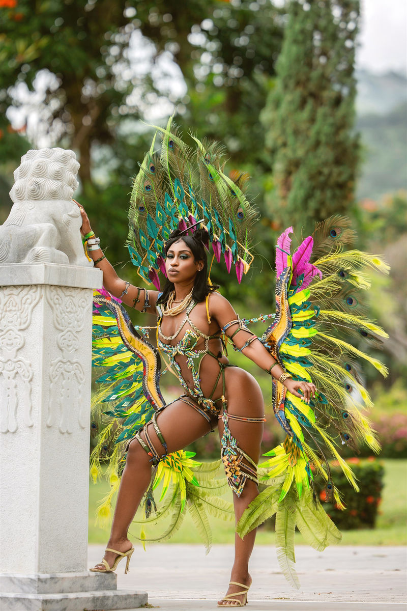 Masquerader in green and yellow feathers beside a stone pillar