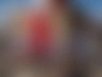 A group of people in patriotic attire participate in a fun run, smiling and holding flags. A red arch and brick building are in the background.