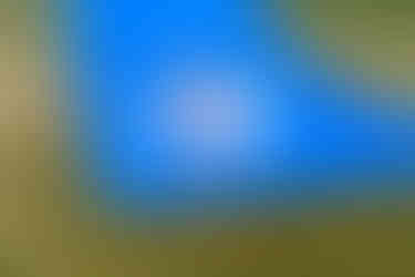 Young girl with red hair splashes into a puddle at the bottom of a bright blue slip-n-slide on a grassy green hill.