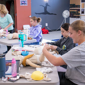 Young women practicing diaper changes on baby dolls at tables