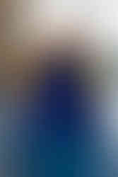 Boy in red swim trunks and goggles climbs across the top of a blue and yellow inflatable structure floating in an indoor pool.