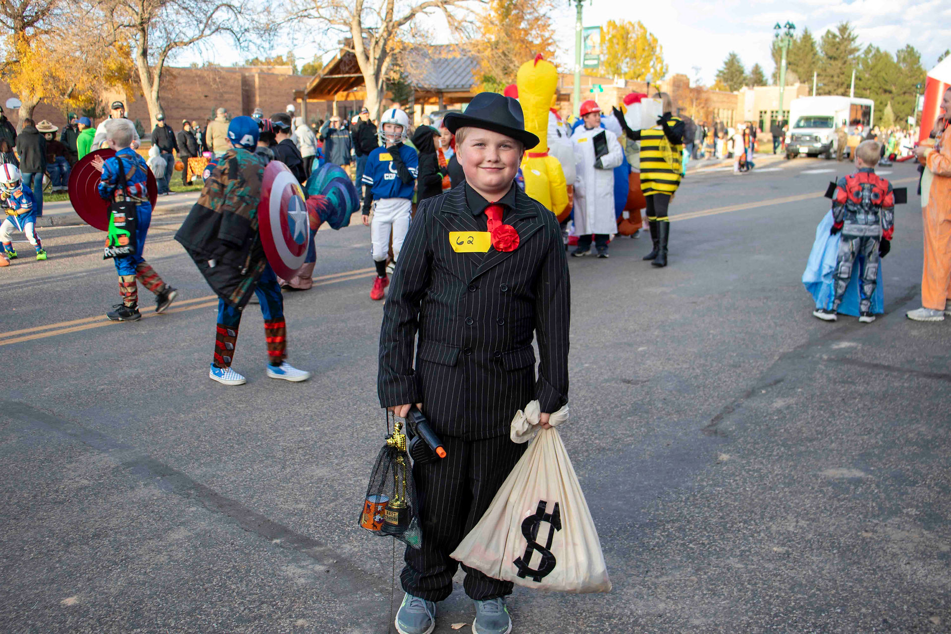 8-11 year costume contest winner Jameson Mlakar. dressed as a gangster with a money bag and nerf gun in a black pinstripe suit with red neckerchief and fedora.