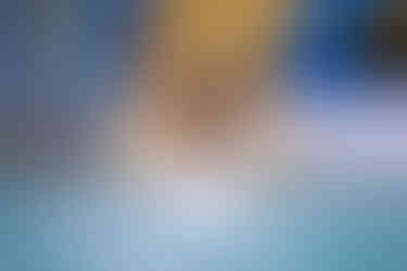 A child in orange swim trunks gets ready to splash into the pool at the bottom of a yellow indoor water slide.