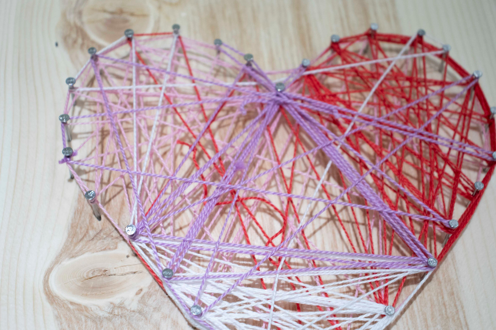 Close up of a string art and nail project in the shape of a heart.