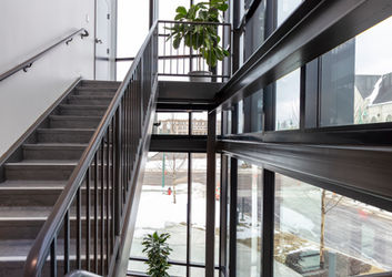 A detailed view of an interior staircase at the Stark Library Operations Center designed by HBM Architects. Floor-to-ceiling windows fill the stairwell with light and create an open atmosphere, complemented by stylish decorative lighting fixtures and potted plants adding fresh greenery to the space.