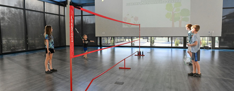 Bright, multi-purpose space with floor-to-ceiling windows, a badminton setup, and a retractable screen, ideal for recreation and events at Afton Ridge.