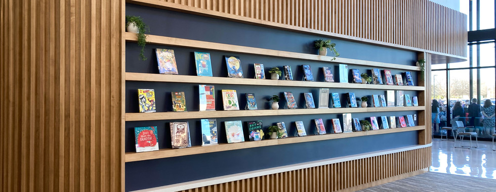 Custom wooden slat feature wall with built-in book displays and greenery, adding warmth and function to the welcoming interior of Afton Ridge Library.