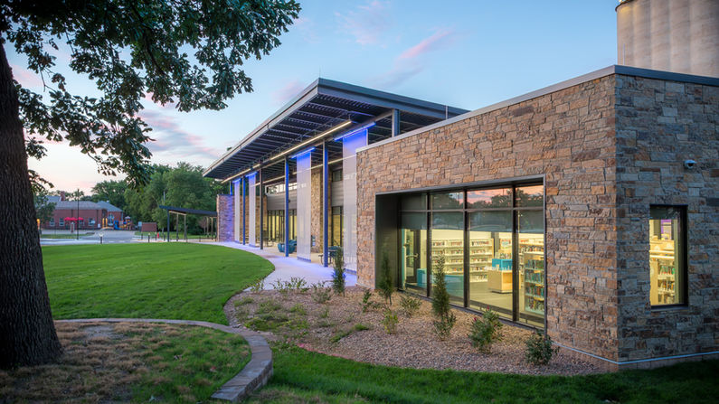 Exterior view of the new Newton Public Library in Newton, Kansas, against a beautiful evening sky. To accomodate multi-purpose use of this facility, colorful light installations have been installed along long panels to provide ambient light to the patio and grassy lawn.