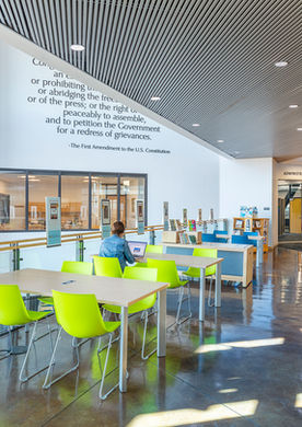 The airy atrium of Rawlings Library in Pueblo, CO, features floor-to-ceiling windows, polished concrete floors, and modern study spaces. Natural light floods the open-concept design, creating a welcoming and functional environment for reading, studying, and community engagement.