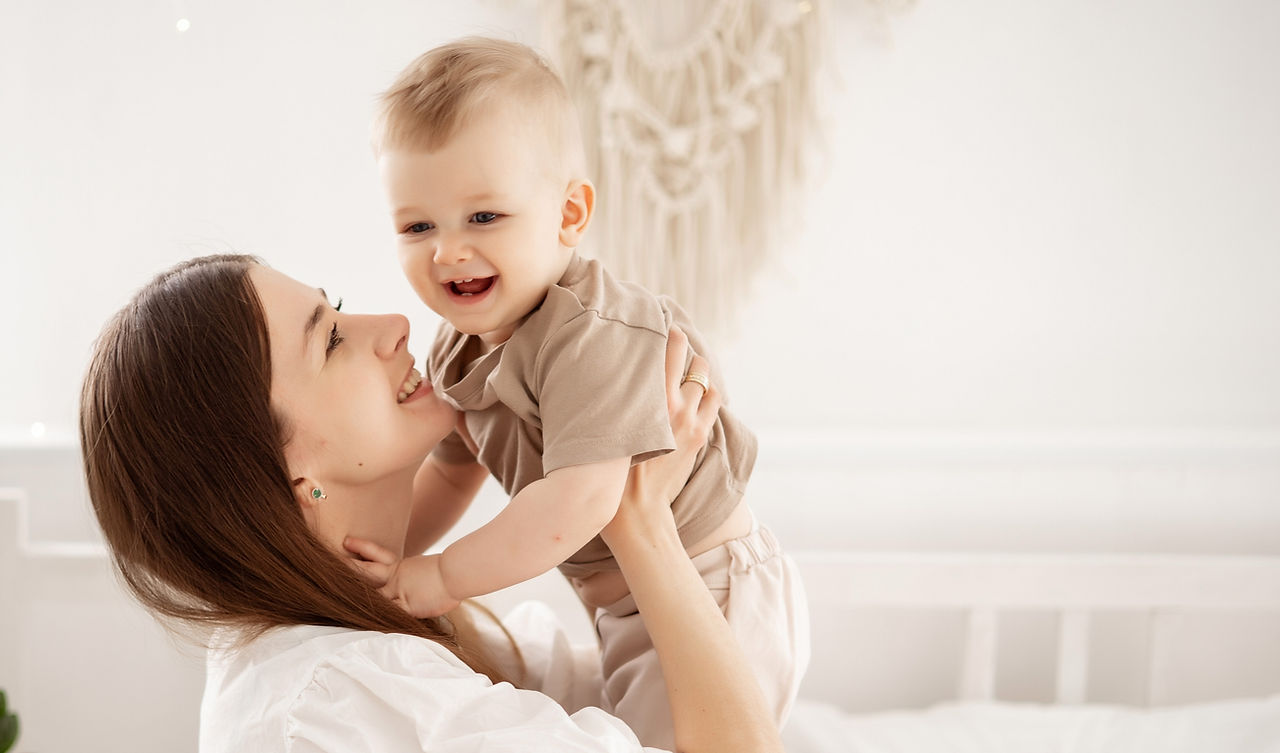 a young beautiful mother with a baby boy hugging on the bed at home in the bedroom, mother