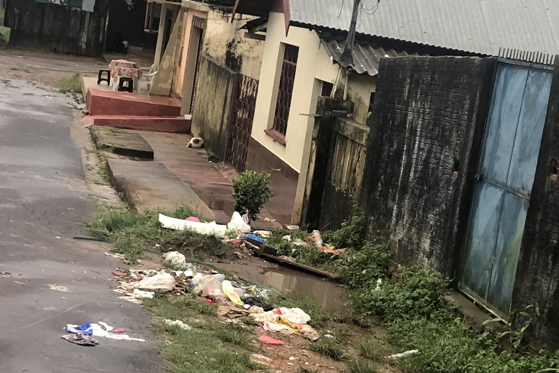 Lixo descartado de forma incorreta em uma rua. Ao fundo, uma série de casas simples e coloridas.
