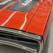 Close-up of orange 1970 Dodge Charger R/T 440 with matte black hood stripes and chrome bumper during windshield protection film service