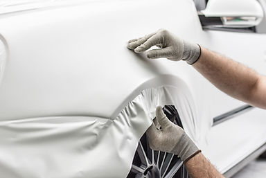 An SUV being wrapped in Satin White Vinyl. The man is working on the wheel well