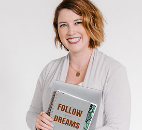 Melissa (white woman with shoulder length red hair) is smiling at the camera and holding a notebook with the phrase "Follow Your Dreams"
