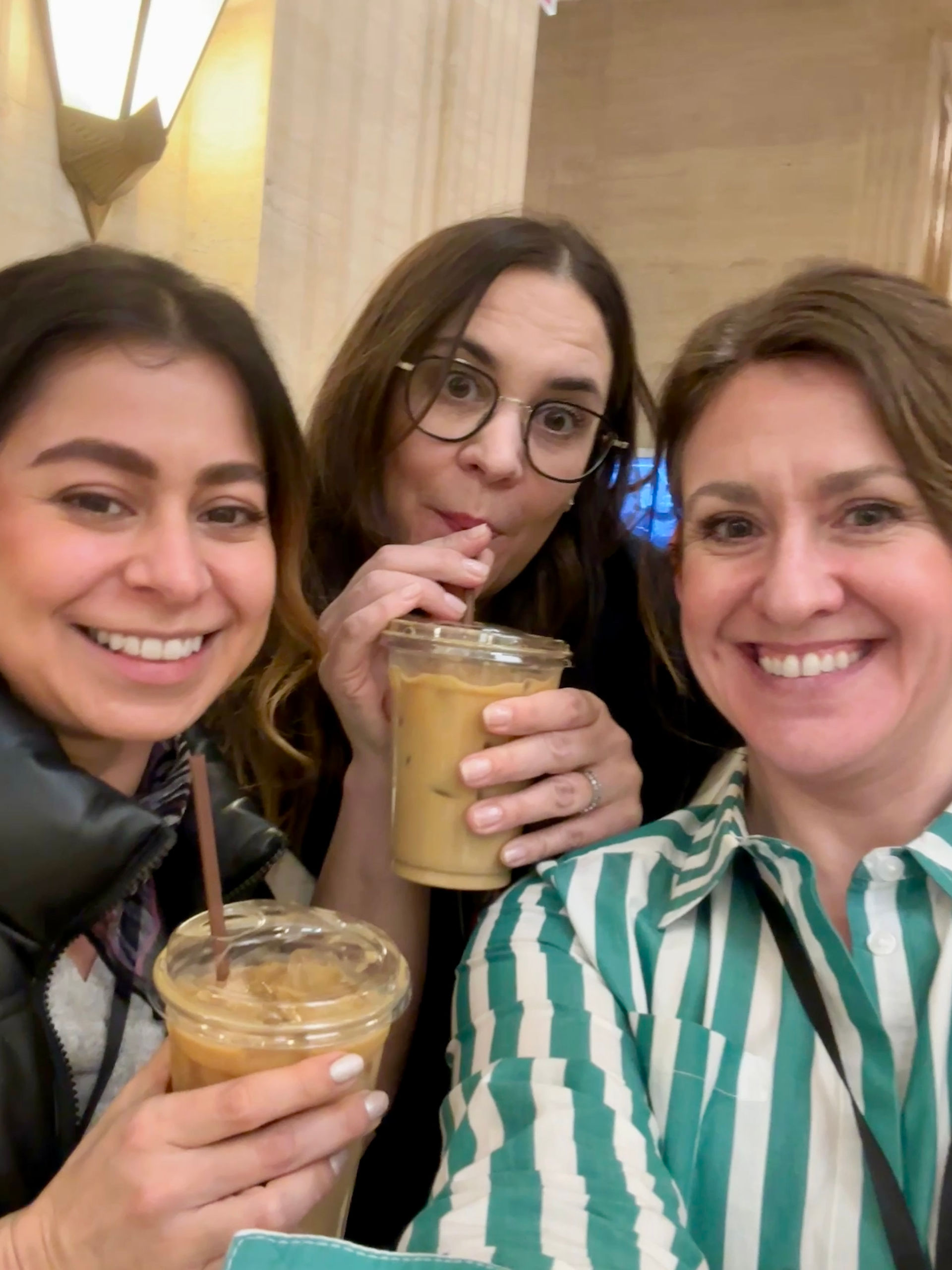 Three women from Amanda’s team holding iced coffees and smiling together during a break at the Merchandise Mart
