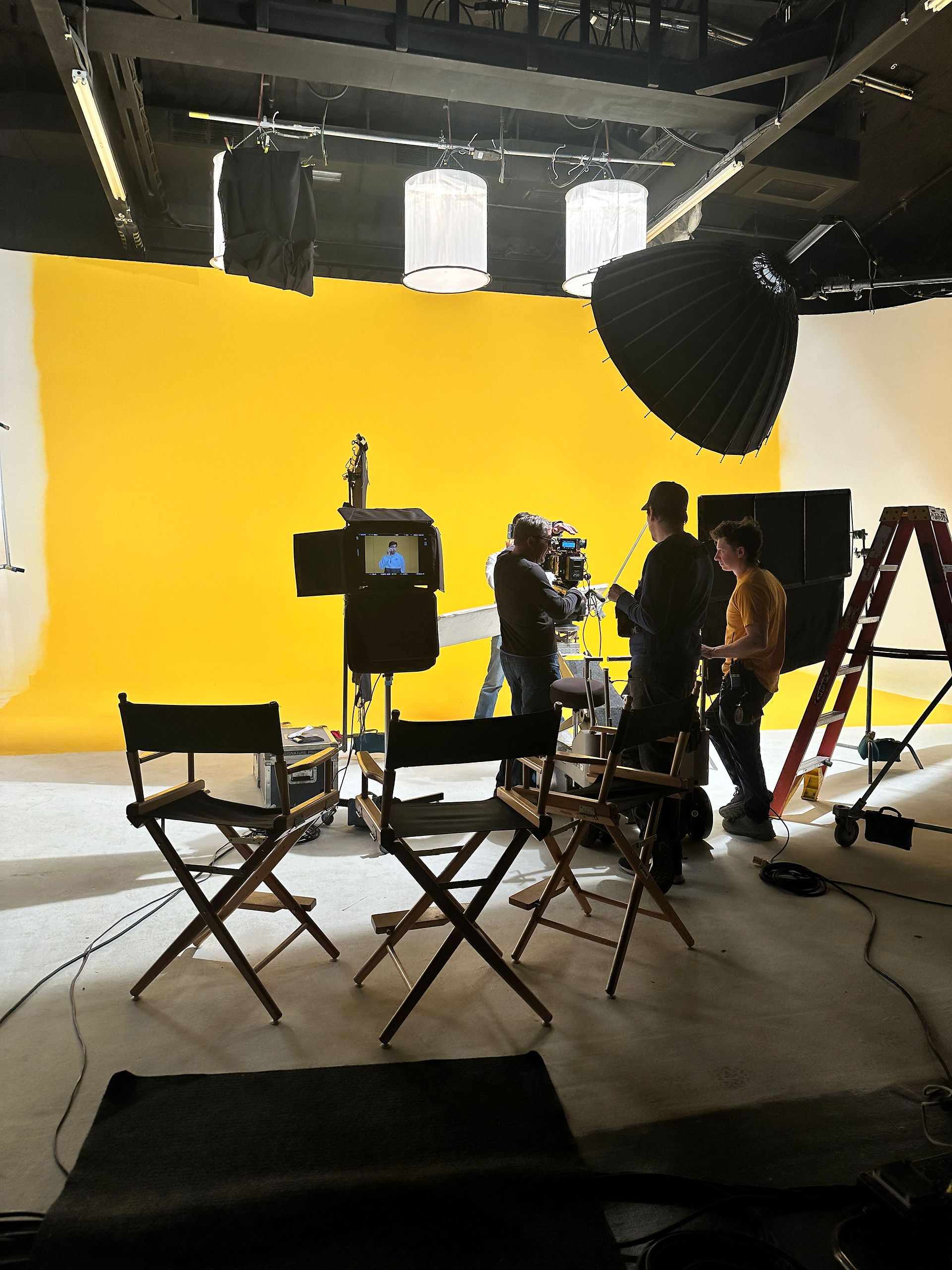 Crew members set up cameras and lighting on a yellow background set for a commercial shoot at Essanay Studios, Chicago.