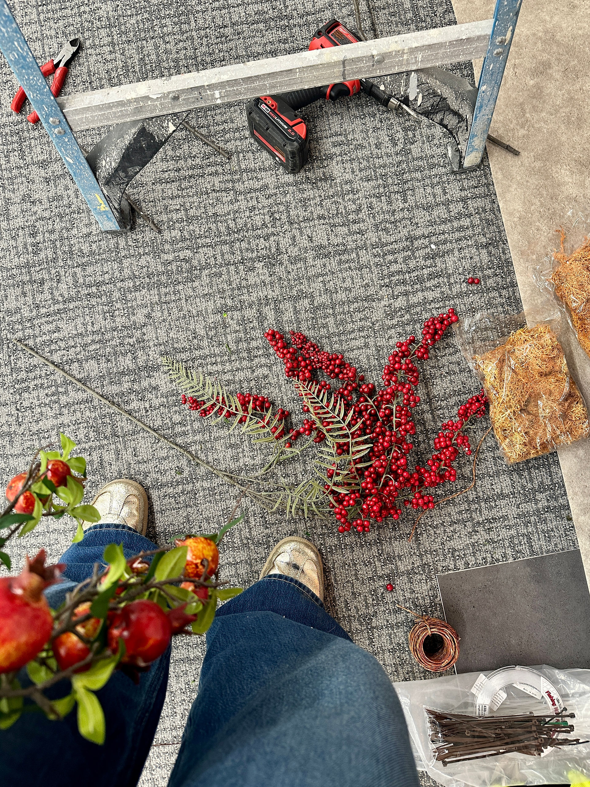 Overhead view of installation materials—berries, tools, and rocks—on the floor during setup.
