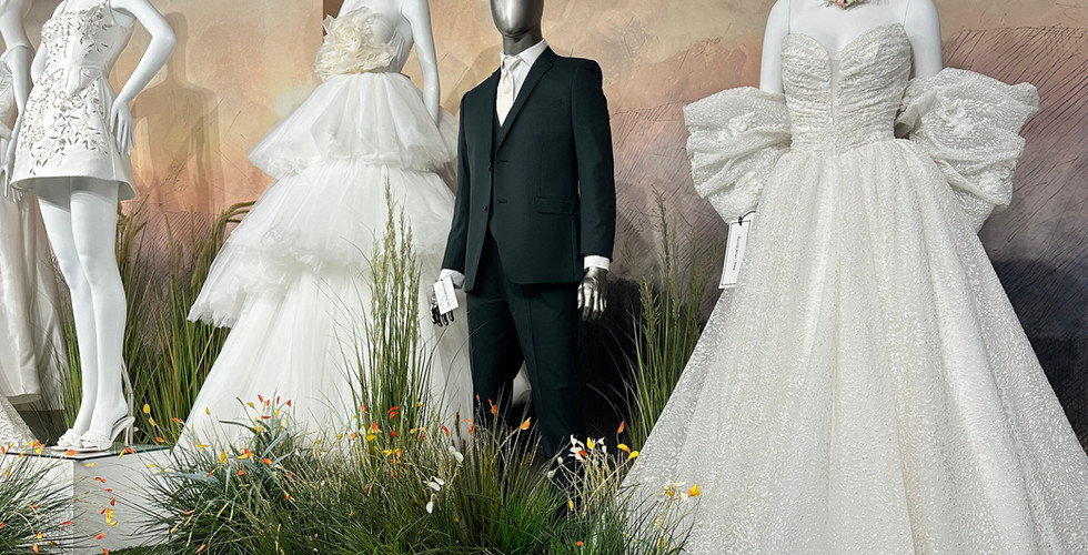 Full group of mannequins in bridal gowns and menswear, arranged at varying heights with greenery to give each look a spotlight moment.