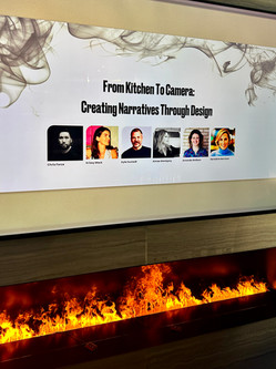 Event signage for the "From Kitchen to Camera: Creating Narratives Through Design" panel, featuring headshots of the panelists, including Chris Force, Krissy Mack, Kyle Hustedt, Aimee Wertepny, Amanda Worsley, and Geraldine Morrison, displayed above a modern fireplace in the Dacor Kitchen Theater at the Merchandise Mart.
