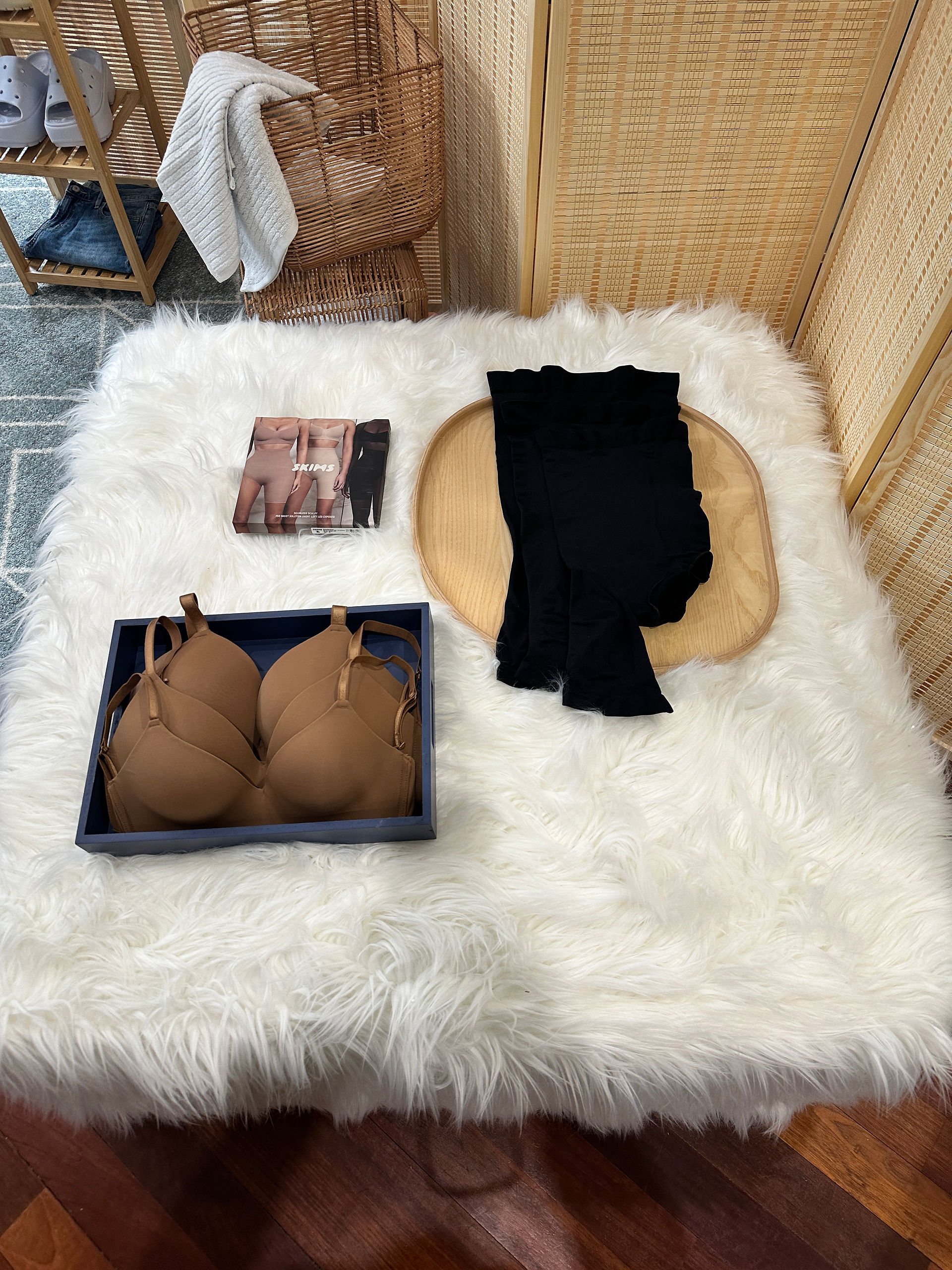 White fluffy rug with black clothing, tan bra, and accessories laid out for display.
