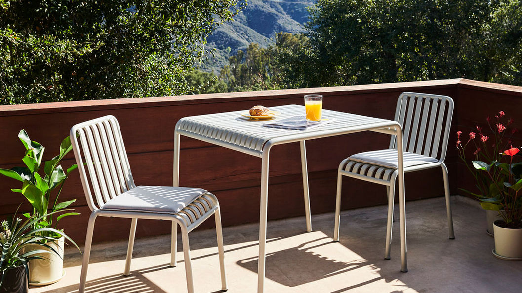 露台上,兩張Palissade椅子圍著一張Palissade 格柵桌,桌上有柳橙汁和糕點。陽光明媚,周圍綠樹成蔭,氣氛悠閒。
