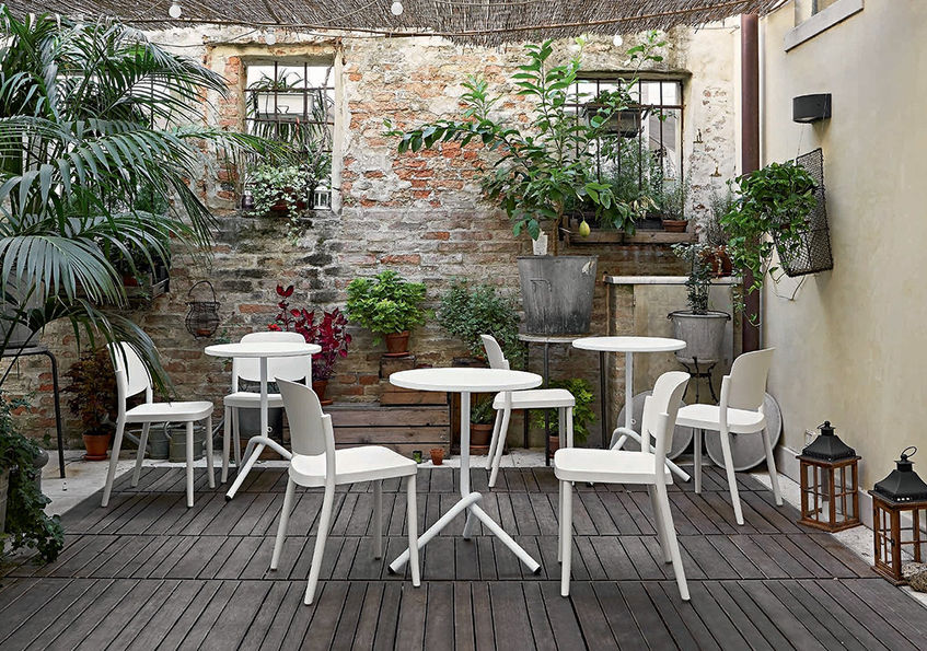 庭院內有幾張TA1白色桌,背景是建築磚牆,上有綠植裝飾,地面為木質地板,適合休閒放鬆。