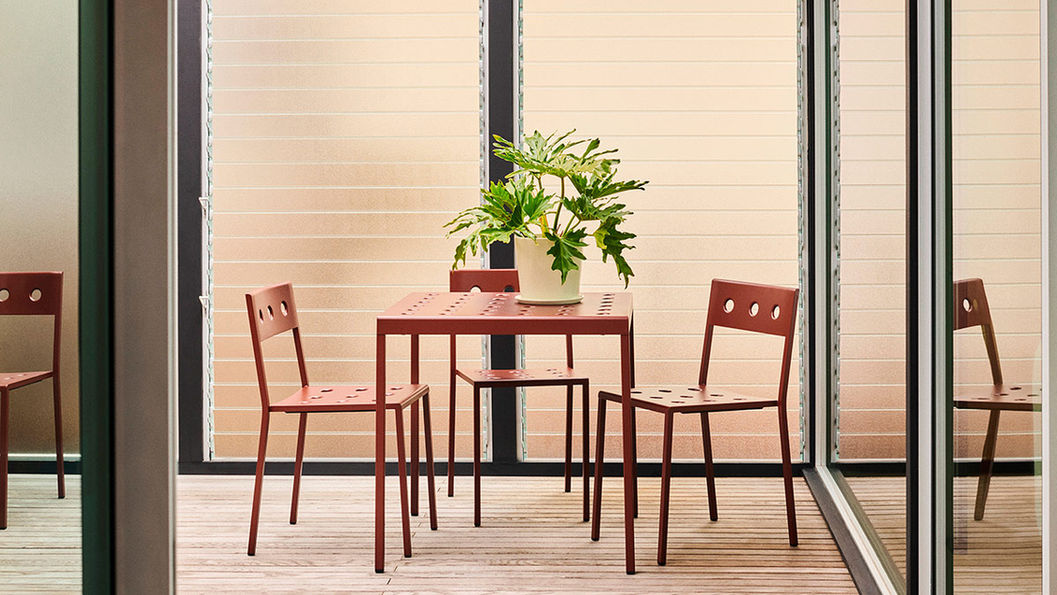 BALCONY 紅色金屬桌椅擺在陽台木地板上,桌上有綠色植物。背景為磨砂玻璃牆,整體簡約現代。