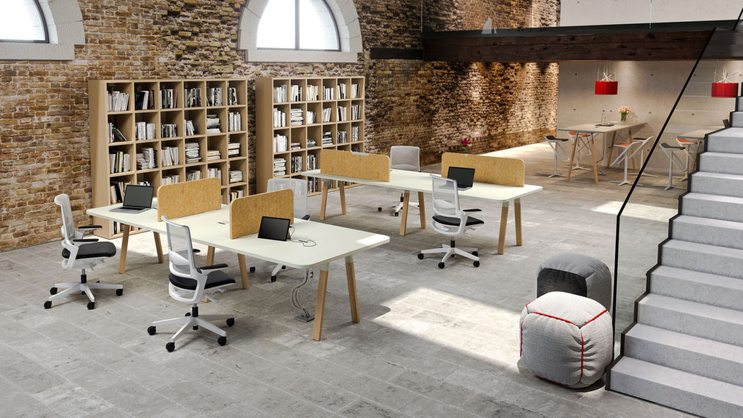 一個兩層樓的開放式辦公室,設計風格結合了工業風與溫馨感。磚牆和挑高天花板營造出loft風格,並搭配淺色的工作站、辦公椅和書櫃,樓梯下方還有一個休息區,整體顯得既現代又舒適。