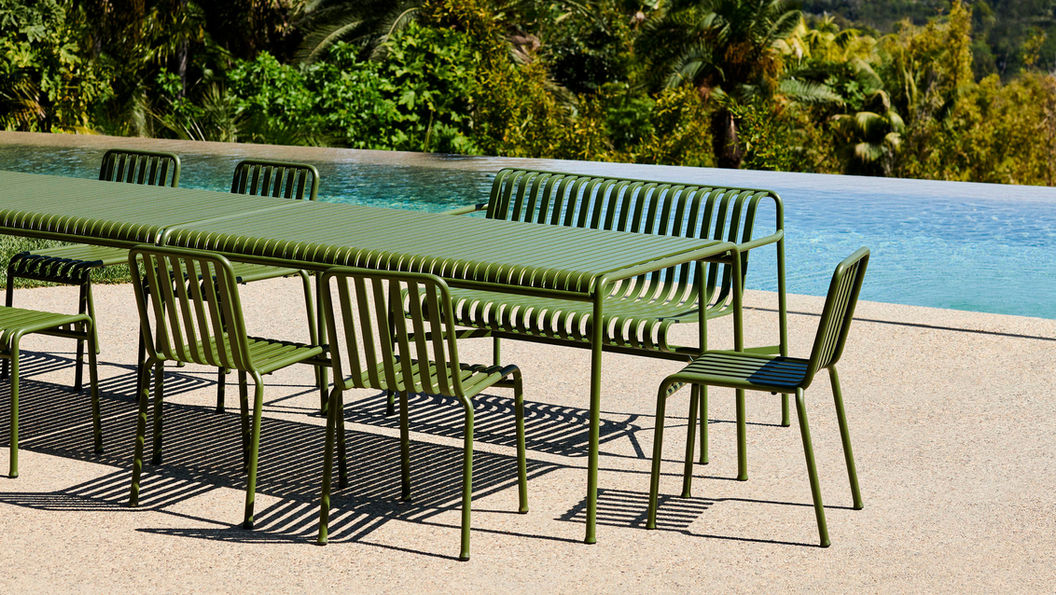 Palissade 綠色金屬椅和 Palissade 格柵桌桌子擺放在泳池邊的戶外休閒區域,背景為鬱鬱蔥蔥的植物與藍色水面,體現寧靜氛圍。