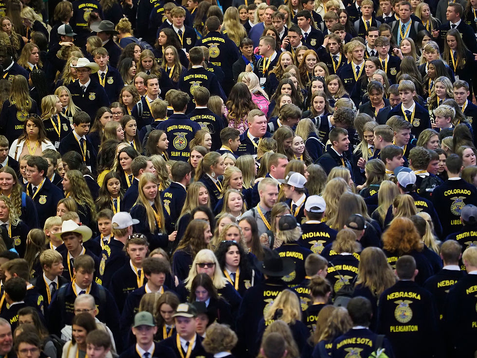 Indoor crowd of teens in navy FFA jackets and yellow lanyards, with state names like South Dakota, Iowa, Nebraska visible.