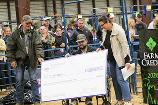 People at a livestock auction hold an oversized check in front of a crowd, with a Farm Credit 2026 sign nearby.
