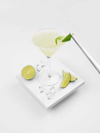 A Margarita cocktail made with El Sueño Tequila and served in a martini glass with lime wedges. 