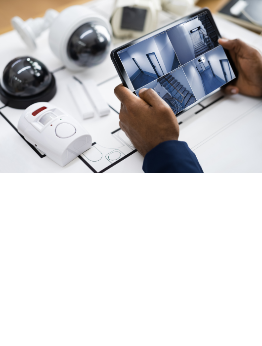 Residential security cameras, alarms on a desk with a person veiwing surveillance feed on an tablet