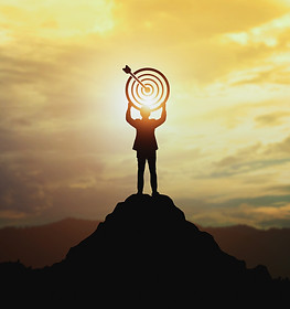 Silhouette of businessman holding a target board on top of mountain. Concept of aim and ob
