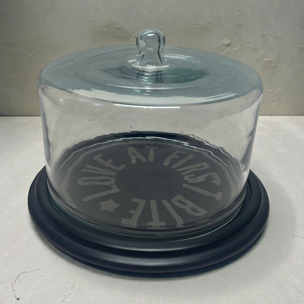 Glass cloche with 'LOVE AT FIRST BITE' text on black marble base; cake dome