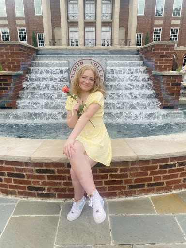 Shae, a blonde woman in a yellow dress, sitting on the fountain edge