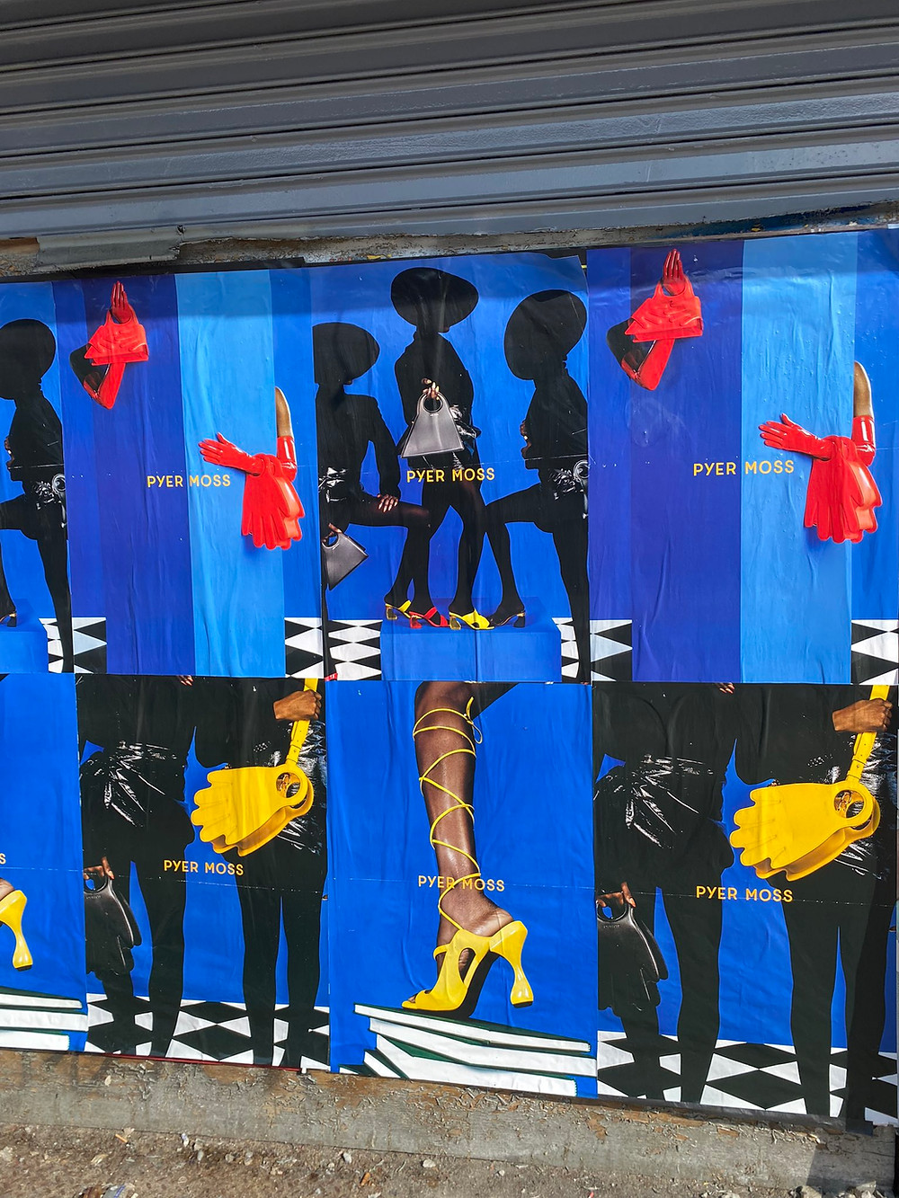 A blue billboard with brightly colored red handbags and gloves and yellow handbags and shoes