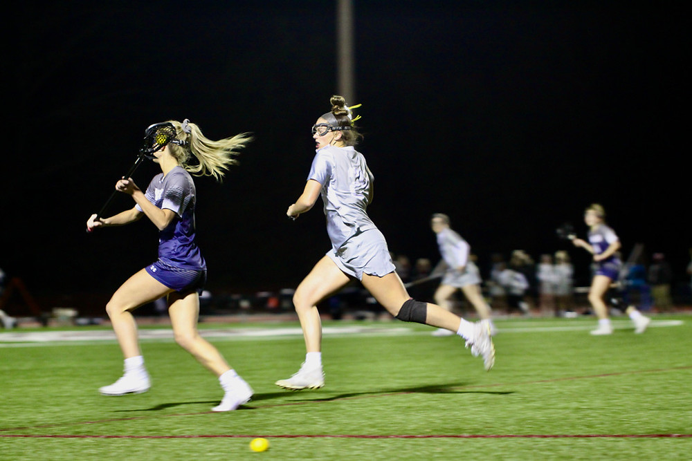 Two lacrosse players run on the field