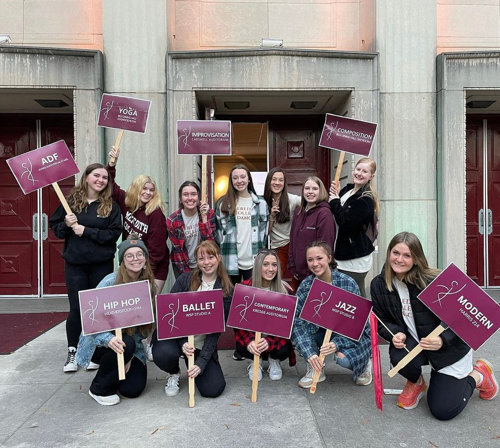People standing in front of Jones Auditorium and holding up maroon signs that have various dance styles listed