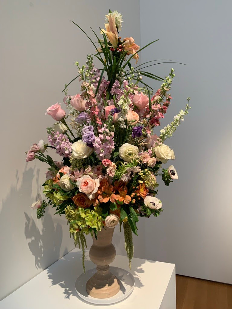 A beige vase with mainly pink flowers and greenery