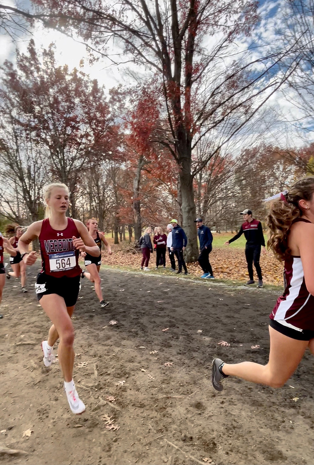 Corrine, a blonde girl in a Meredith jersey and with a number taped to her chest, running on a dirt path at nationals