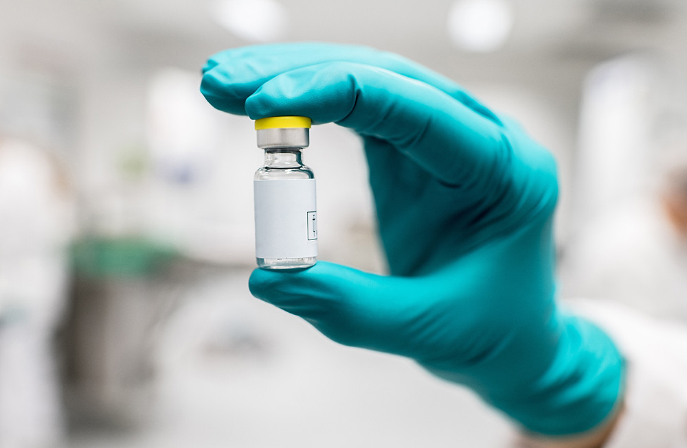A gloved hand holding a COVID-19 vaccine vial