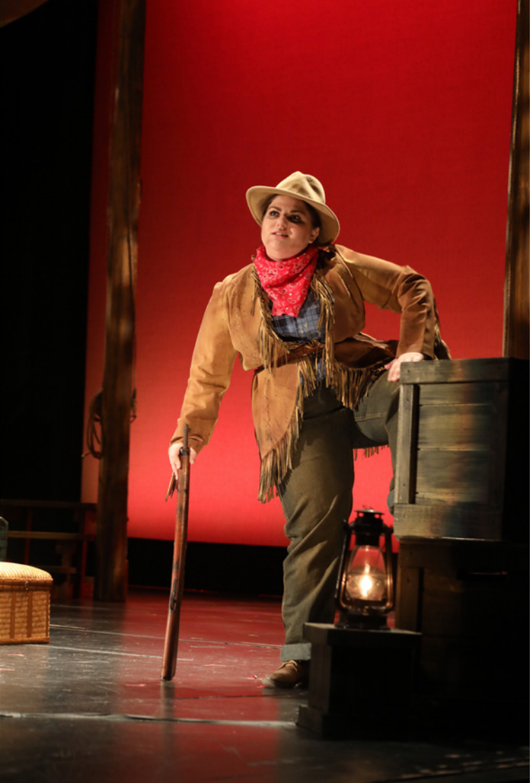 A girl dressed in Old West clothes on a stage with a red background