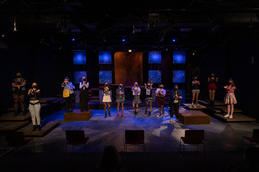 A dark stage with blue backlighting and actors standing in a line onstage