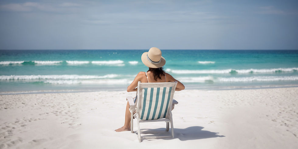 relaxed middle aged female sitting on white chair on white sand beach facing sea.jpg