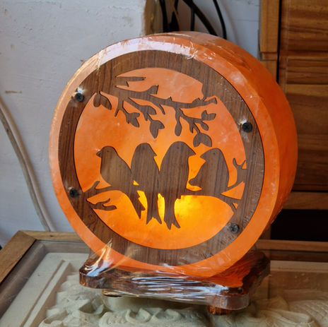 Lámpara de sal rosa del Himalaya circular con frontal de madera tallada con silueta de pájaros en una rama