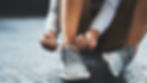 Person tying gray sneakers on a textured floor. Focus on hands and shoes. Calm and focused mood with natural lighting.